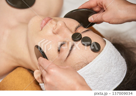 Young Caucasian Female Enjoying Relaxing Hot Stone Facial Massage For Skin Rejuvenation And Stress Young Caucasian Female Enjoying Relaxing Hot Stone Facial Massage For Skin Rejuvenation And Stress 137009034