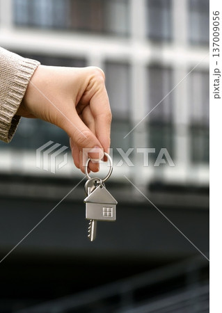 Vertical closeup Woman Holds House Shaped Key, Real Estate Agent Facilitates Transfer. Modern Apartment Building, Ownership, Purchase, Investment, Relocation. Sale Buy Apartment. Vertical closeup Woman Holds House Shaped Key, Real Estate Agent Facilitates Transfer. Modern Apartment Building, Ownership, Purchase, Investment, Relocation. Sale Buy Apartment. 137009056