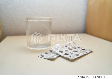 Glass of water and empty pill blisters on white table representing health and medication concepts Glass of water and empty pill blisters on white table representing health and medication concepts 137009125
