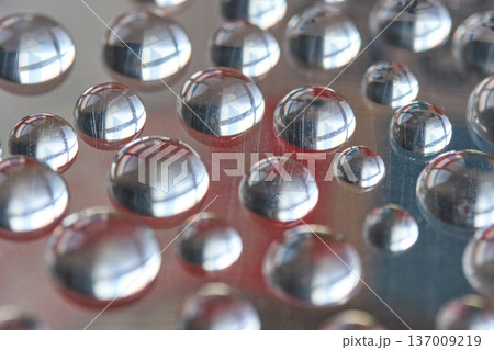 Close-up of reflective water droplets on smooth surface capturing light and colorful abstract 137009219
