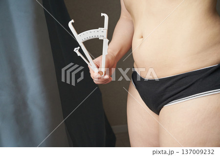 Young caucasian female using skinfold caliper for body fat measurement in health assessment Young caucasian female using skinfold caliper for body fat measurement in health assessment 137009232