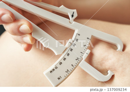 Female using skinfold caliper for body fat measurement, close-up of caucasian hand and caliper Female using skinfold caliper for body fat measurement, close-up of caucasian hand and caliper 137009234