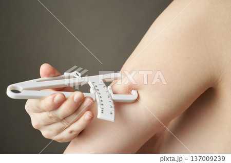 Female hands using skinfold caliper for body fat measurement on arm close-up 137009239