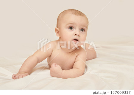 Caucasian Infant Lying On White Bed With Curious Expression, Portrait Of Cute Baby Boy Exploring Caucasian Infant Lying On White Bed With Curious Expression, Portrait Of Cute Baby Boy Exploring 137009337