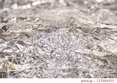 Crumpled silver aluminum foil texture with shiny reflective surface and abstract pattern 137009353