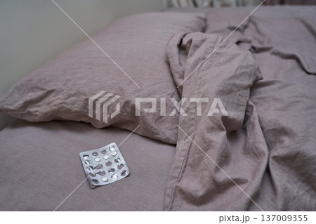 Unmade bed with empty blister pack on pink sheets depicting neglect and anxiety Unmade bed with empty blister pack on pink sheets depicting neglect and anxiety 137009355