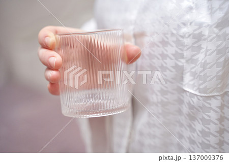 Caucasian female holding clear glass tumbler wearing white patterned shirt indoors elegance Caucasian female holding clear glass tumbler wearing white patterned shirt indoors elegance 137009376