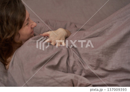 Caucasian female adult relaxing in bed under purple linen blanket smiling comfortably 137009393