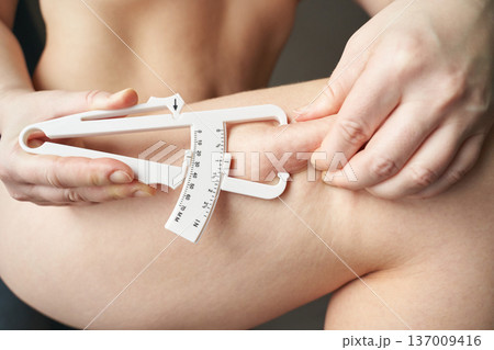 Female adult measuring body fat with caliper on thigh for fitness and health assessment Female adult measuring body fat with caliper on thigh for fitness and health assessment 137009416