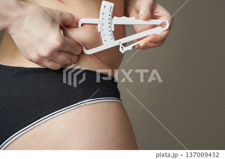 Young caucasian female measuring body fat with caliper in fitness and health concept image 137009432