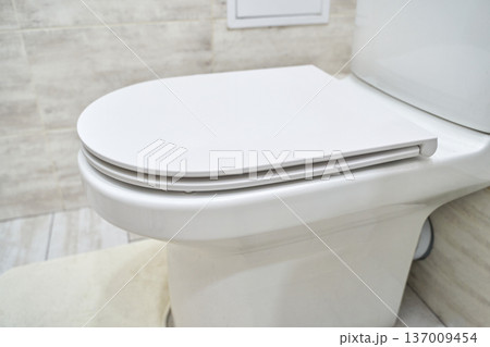 Modern white toilet with closed seat in minimalist bathroom with tile floor Modern white toilet with closed seat in minimalist bathroom with tile floor 137009454