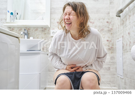Caucasian female adult experiencing pain in bathroom setting, expressing discomfort and tension Caucasian female adult experiencing pain in bathroom setting, expressing discomfort and tension 137009466