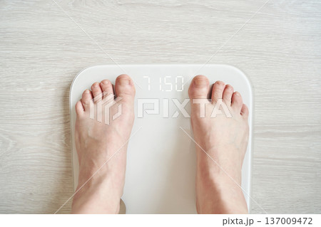 Caucasian adult feet on digital scale displaying weight on light wood floor for health and fitness Caucasian adult feet on digital scale displaying weight on light wood floor for health and fitness 137009472