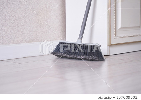 Close-up of broom sweeping dust on hardwood floor in a modern clean home interior setting 137009502