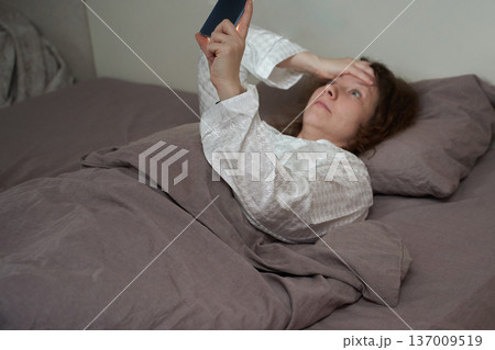 Caucasian mature female awake in bed using smartphone at night, anxiety and sleeplessness concept Caucasian mature female awake in bed using smartphone at night, anxiety and sleeplessness concept 137009519