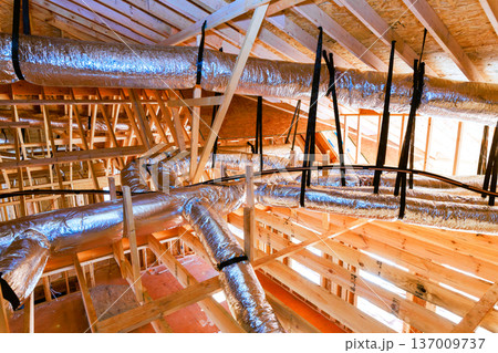 Workers install ductwork in ceiling of building that is under construction is wooden beams 137009737