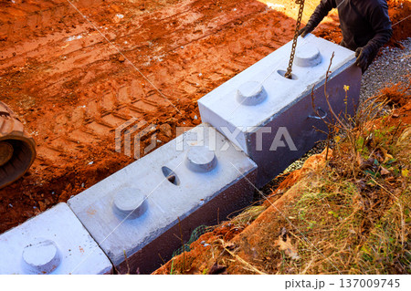 Construction worker uses chain to lift concrete blocks on building site with to place it at retaining walls 137009745