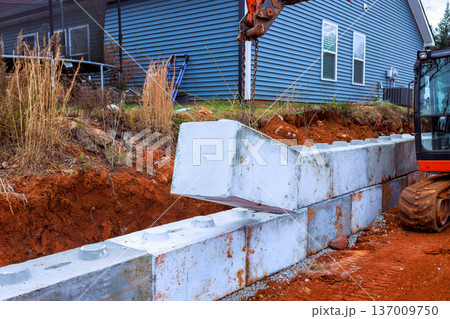 Workers use excavator machinery to position concrete blocks for retaining wall at home site Workers use excavator machinery to position concrete blocks for retaining wall at home site 137009750