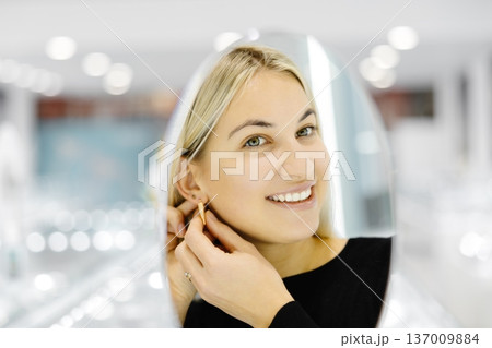 Happy woman trying on gold earrings in jewelry store Happy woman trying on gold earrings in jewelry store 137009884