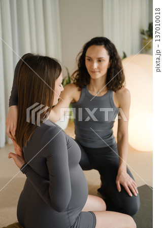 Two women practice yoga together in a bright indoor space with soft lighting in the morning, focusing on connection and support during pregnancy Two women practice yoga together in a bright indoor space with soft lighting in the morning, focusing on connection and support during pregnancy 137010018