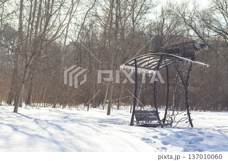 A handcrafted wrought iron garden swing, designed with an ornate frame and artistic top detailing, situated in a snowy outdoor setting. Outdoor A handcrafted wrought iron garden swing, designed with an ornate frame and artistic top detailing, situated in a snowy outdoor setting. Outdoor 137010060