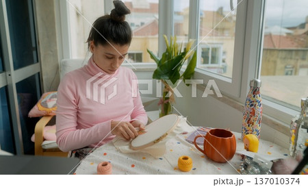 Focused woman crafting intricate embroidery under daylight Focused woman crafting intricate embroidery under daylight 137010374