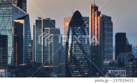 United Kingdom, London: Illuminated London skyline at sunset featuring iconic skyscrapers like the Gherkin and modern architecture of the financial district. Drone flight United Kingdom, London: Illuminated London skyline at sunset featuring iconic skyscrapers like the Gherkin and modern architecture of the financial district. Drone flight 137010415
