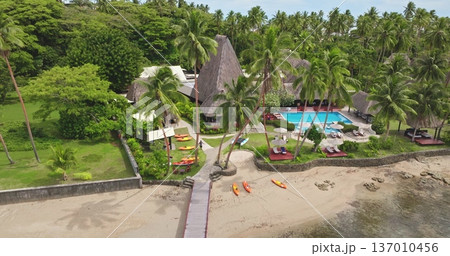 Tropical resort on Fiji Savusavu bay with palm-fringed sandy beach, pool and thatched bungalows under bright sky, kayaks at the waterfront for a luxury island getaway Tropical resort on Fiji Savusavu bay with palm-fringed sandy beach, pool and thatched bungalows under bright sky, kayaks at the waterfront for a luxury island getaway 137010456