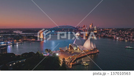 Australia, Sydney: Sydney Harbour at sunset, illuminated Sydney Opera House and Harbour Bridge against vibrant sky. Breathtaking aerial view of modern city skyline at night. Drone flight Australia, Sydney: Sydney Harbour at sunset, illuminated Sydney Opera House and Harbour Bridge against vibrant sky. Breathtaking aerial view of modern city skyline at night. Drone flight 137010563