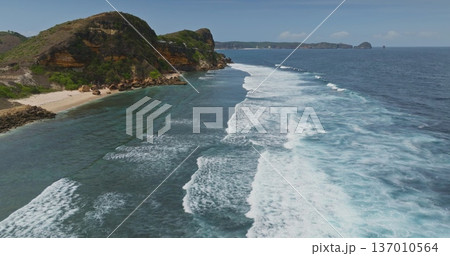 Lombok Bukit Merese coastline beach with rugged cliffs and sandy beach meeting the clear calm turquoise water, with powerful ocean waves breaking parallel to the shore. Aerial view drone 137010564