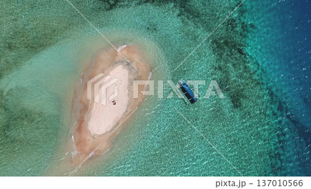 Tiny sandbar in turquoise waters of Lombok with traditional outrigger boat moored nearby, aerial drone view of pristine, tranquil tropical island escape perfect for snorkeling. Exotic nature, top down Tiny sandbar in turquoise waters of Lombok with traditional outrigger boat moored nearby, aerial drone view of pristine, tranquil tropical island escape perfect for snorkeling. Exotic nature, top down 137010566
