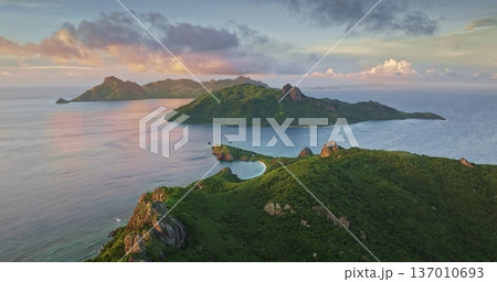 Fiji Yasawa tropical Islands archipelago features lush green volcanic mountains alongside pristine sandy beach and turquoise tropical ocean waters under a vibrant sunset sky. Aerial drone flight Fiji Yasawa tropical Islands archipelago features lush green volcanic mountains alongside pristine sandy beach and turquoise tropical ocean waters under a vibrant sunset sky. Aerial drone flight 137010693