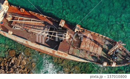Tourist destination Edro III shipwreck resting on rocky shore, rusty hull contrasting with the clear turquoise waters of Mediterranean Sea, aerial zoom out drone perspective. Travel to Paphos, Cyprus 137010800