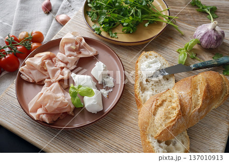 High-quality farm food on wooden cutting board. Top view. Flat lay photo. Soft goat cheese on bread, basil and mortadella sandwich. Italian tradition cuisine. High-quality farm food on wooden cutting board. Top view. Flat lay photo. Soft goat cheese on bread, basil and mortadella sandwich. Italian tradition cuisine. 137010913