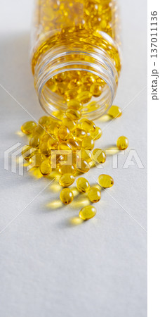 Yellow softgel scattered from transparent jar on greige ston, Nutritional supplements or vitamins Yellow softgel scattered from transparent jar on greige ston, Nutritional supplements or vitamins 137011136