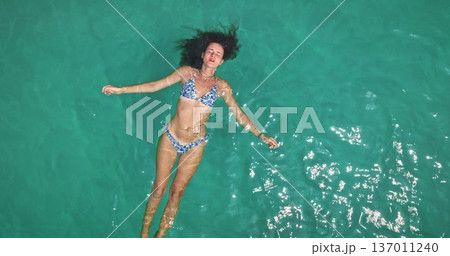 Beautiful young woman enjoy tranquility, floating on her back in clear turquoise ocean water, relaxing under sun during tropical vacation to Koh Lanta, Thailand. Aerial top down panorama zoom out Beautiful young woman enjoy tranquility, floating on her back in clear turquoise ocean water, relaxing under sun during tropical vacation to Koh Lanta, Thailand. Aerial top down panorama zoom out 137011240