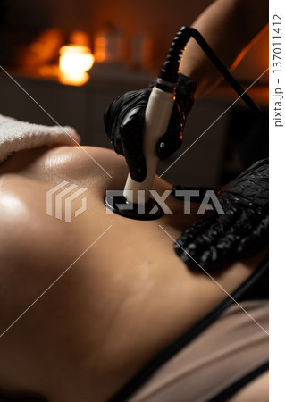 Professional performing radiofrequency body contouring on woman's abdomen for non-invasive skin tightening and rejuvenation, clinic setting Professional performing radiofrequency body contouring on woman's abdomen for non-invasive skin tightening and rejuvenation, clinic setting 137011412