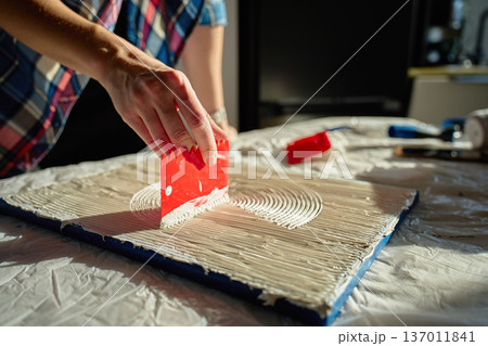Hand pressing red plastic scraper into thick paste to create concentric textured lines 137011841