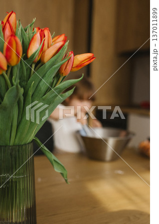 Little girl mixing dough in bowl while mother cooking in background, family baking together at home kitchen Little girl mixing dough in bowl while mother cooking in background, family baking together at home kitchen 137011899