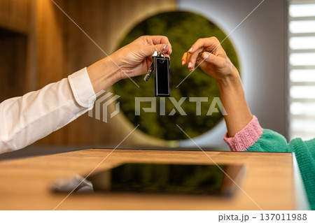 Hotel receptionist handing room key to guest at reception desk close up 137011988