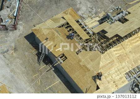 Aerial view of builders working on unfinished residential house with wooden roof frame structure under construction in Florida suburban area Aerial view of builders working on unfinished residential house with wooden roof frame structure under construction in Florida suburban area 137013112
