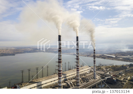 Tall pipes of power plant, white smoke on rural landscape, lake water and blue sky copy space background. Tall pipes of power plant, white smoke on rural landscape, lake water and blue sky copy space background. 137013134