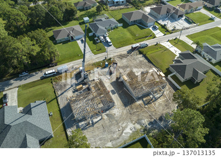 Aerial view of lifting crane and builders working on unfinished residential house with wooden roof frame structure under construction in Florida suburban area Aerial view of lifting crane and builders working on unfinished residential house with wooden roof frame structure under construction in Florida suburban area 137013135
