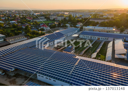 Aerial view of solar power plant with blue photovoltaic panels mounted on industrial building roof for producing green ecological electricity at sunset. Production of sustainable energy concept Aerial view of solar power plant with blue photovoltaic panels mounted on industrial building roof for producing green ecological electricity at sunset. Production of sustainable energy concept 137013148