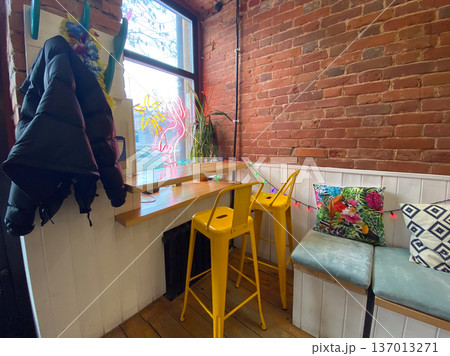 Cozy cafe corner with colorful pillows and wooden furniture. Relaxed social atmosphere, urban comfort, and creative interior design with eclectic details. 137013271