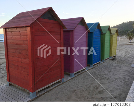 Colorful wooden beach cabins aligned on sandy shore. Coastal tourism, summer vacation and seaside leisure concept 137013308