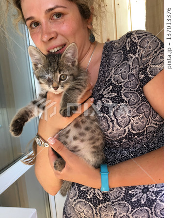 Woman holding kitten with injured eye indoors. Care, rescue, compassion and responsibility toward animal concept 137013376