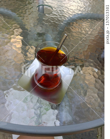 Glass of black turkish tea on table in cafe setting. Relaxation, pause, hospitality and daily ritual Glass of black turkish tea on table in cafe setting. Relaxation, pause, hospitality and daily ritual 137013381