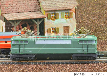 Detailed model train locomotive with pantograph and miniature village background. A close-up view of a green model electric locomotive with a detailed SNCF marking and pantograph, set against a 137013457