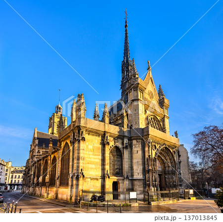 Scenic sunny view of the historic gothic stone architecture, intricate portal, and tall spire of the Saint-Laurent church bathed in warm light in Paris, France. Scenic sunny view of the historic gothic stone architecture, intricate portal, and tall spire of the Saint-Laurent church bathed in warm light in Paris, France. 137013845